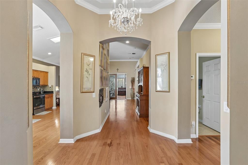 A foyer with hardwood floors leads to a kitchen and a hallway with a chandelier — 4761 WHISPERING WIND AVENUE, TAMPA, FL