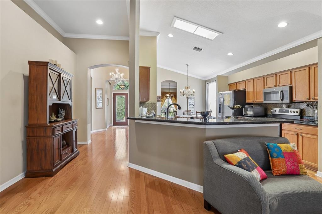 A view of a kitchen with wood cabinets and a breakfast bar facing a living area — 4761 WHISPERING WIND AVENUE, TAMPA, FL