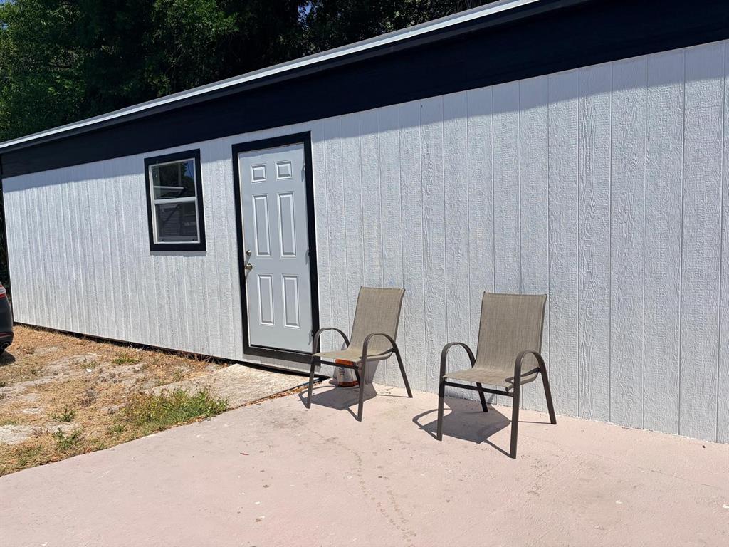 A white exterior wall with a door, a window, and two chairs on a patio — 1304 WINDSOR WAY, TAMPA, FL
