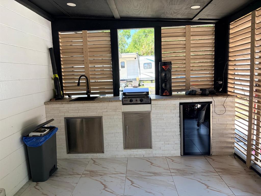 An outdoor kitchen features a stone-tiled counter, a sink, a grill, and a small refrigerator — 1304 WINDSOR WAY, TAMPA, FL