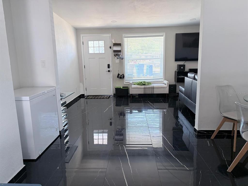 A living room features black marble-look tile flooring, a white front door, and a television — 1304 WINDSOR WAY, TAMPA, FL