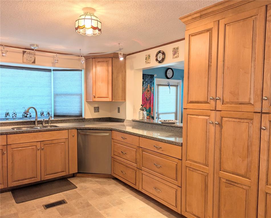 A kitchen features light wood cabinets, granite countertops, a stainless steel dishwasher, and tile flooring — 526 CASSANDRA LANE, LAKELAND, FL