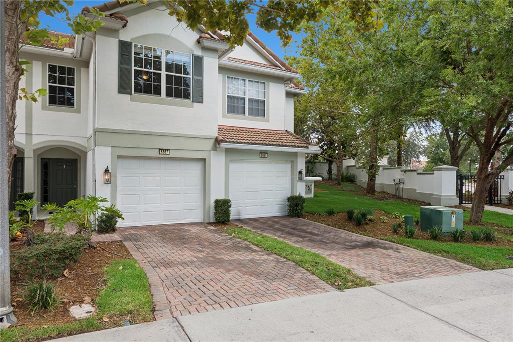 A two-story townhouse with a brick driveway, two garage doors, and a small front lawn — 6887 SPERONE STREET, ORLANDO, FL