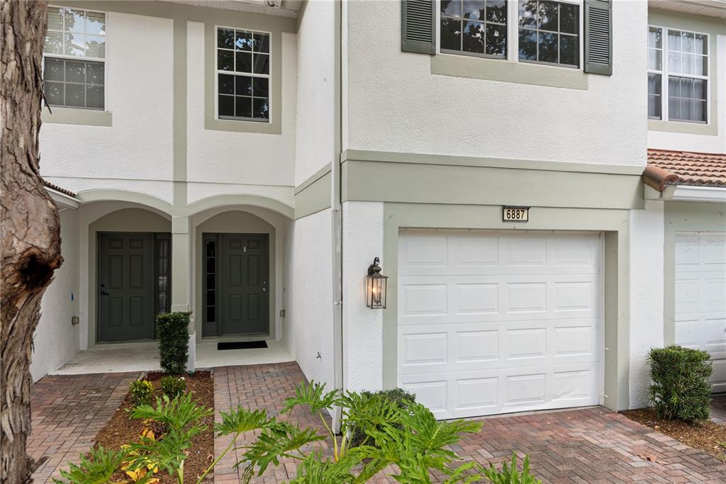A two-story townhouse exterior features a white garage, gray front doors, and brick pavers — 6887 SPERONE STREET, ORLANDO, FL