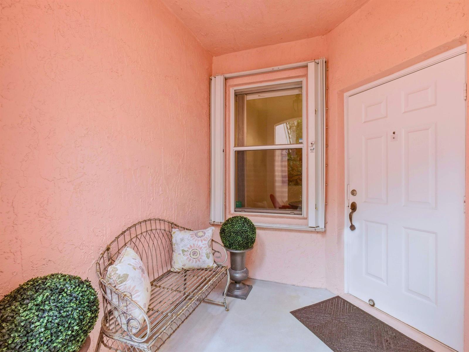 A pink-walled entryway features a metal bench, a window with shutters, and a white door — 308 Coral Trace Court, Delray Beach FL 33445, DELRAY BEACH, FL