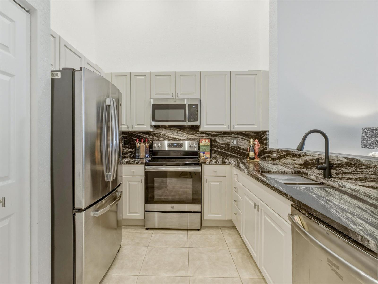 A kitchen features stainless steel appliances, light gray cabinets, and dark, dramatic granite countertops — 308 Coral Trace Court, Delray Beach FL 33445, DELRAY BEACH, FL