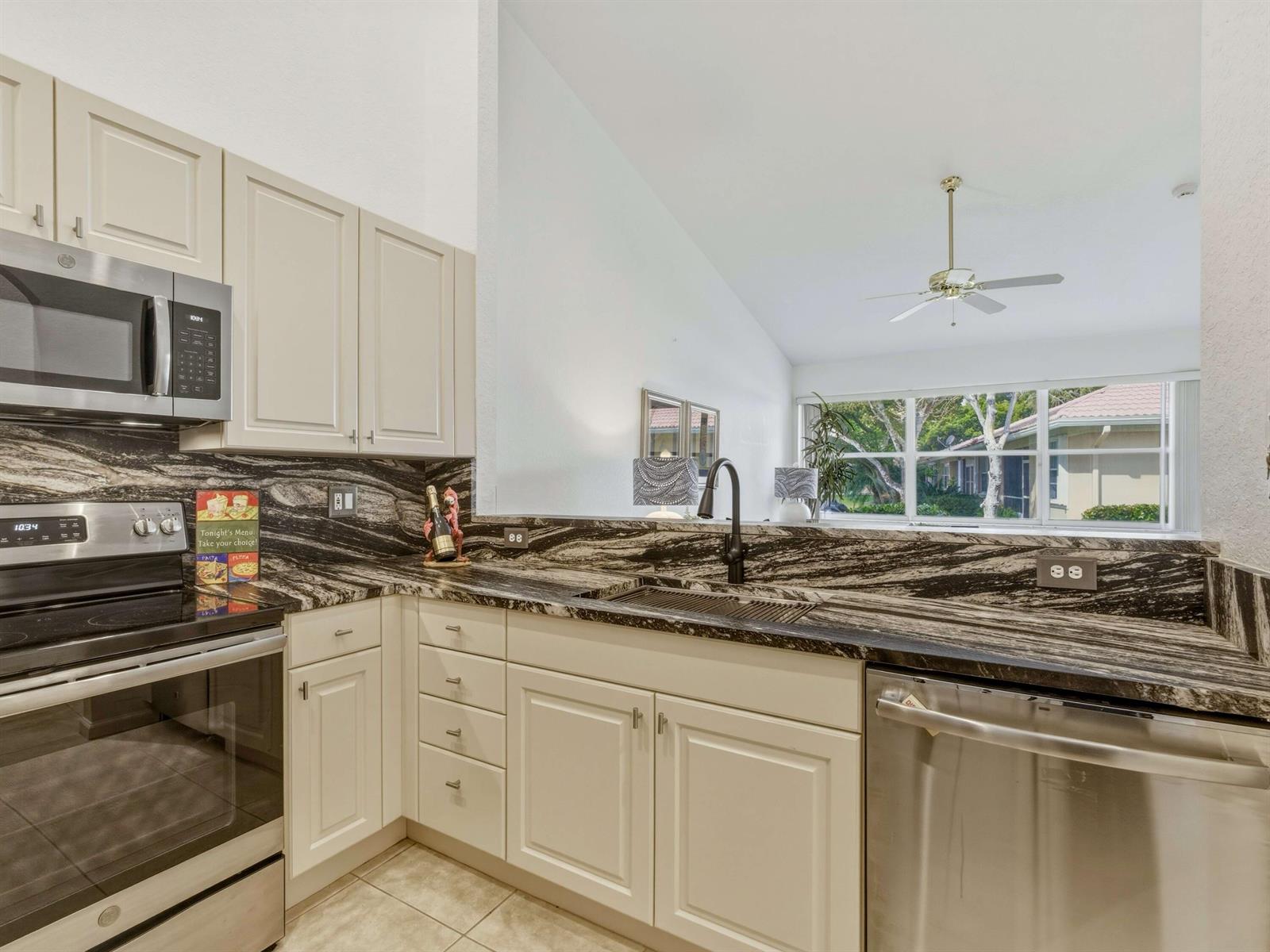 A kitchen with cream cabinets, stainless steel appliances, and dark, dramatic veined granite countertops — 308 Coral Trace Court, Delray Beach FL 33445, DELRAY BEACH, FL