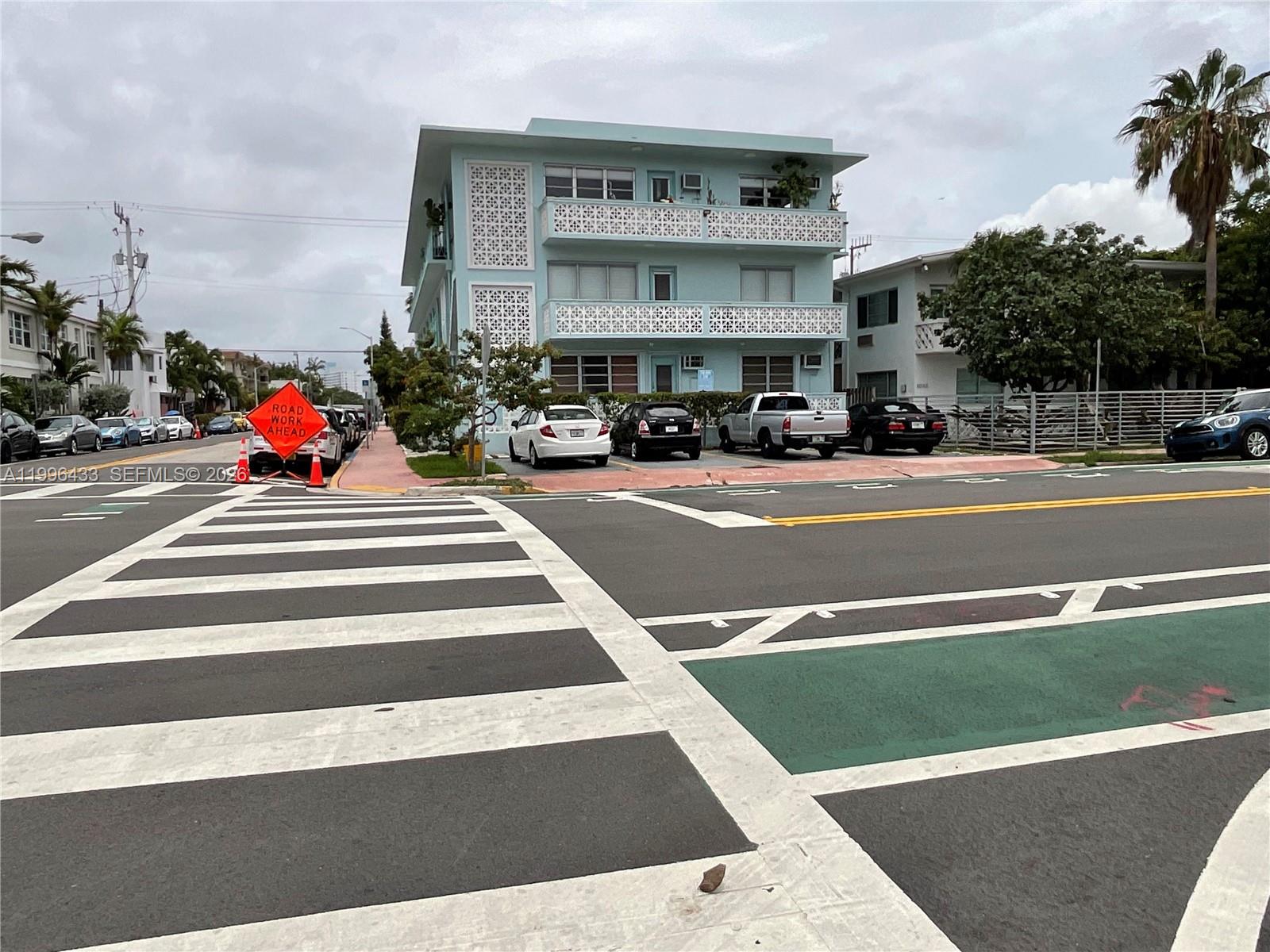 A three-story light blue apartment building sits behind a crosswalk and parked cars — 1004 Pennsylvania Ave # 15, Miami Beach FL 33139, MIAMI BEACH, FL