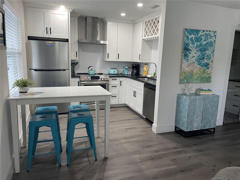 A kitchen features white cabinets, stainless steel appliances, a patterned backsplash, and a breakfast table — 1910 MORRILL STREET UNIT 1, SARASOTA, FL