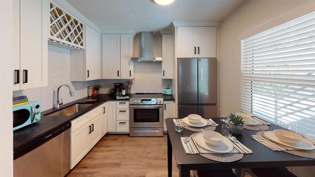 A kitchen features white cabinets, stainless steel appliances, a patterned backsplash, and a dining table — 1910 MORRILL STREET UNIT 1, SARASOTA, FL