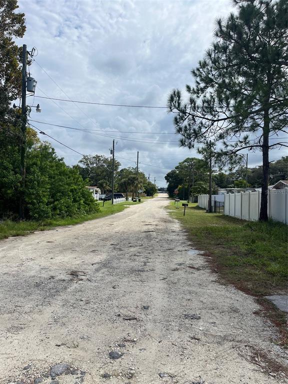 A gravel road stretches into the distance, flanked by trees, utility poles, and a white fence — 7103 JEANNE AVENUE, HUDSON, FL