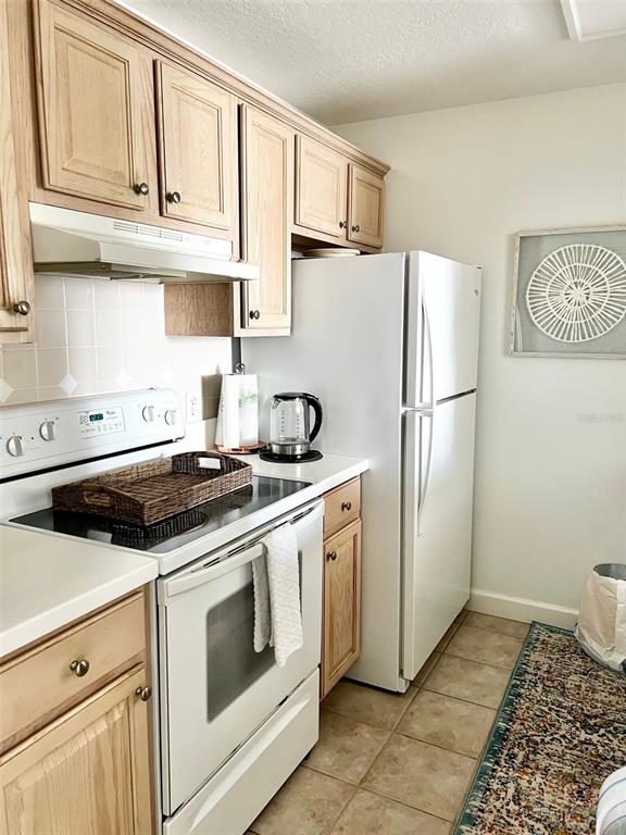 A kitchen features light wood cabinets, white appliances, a tiled backsplash, and a patterned area rug — 750 N TAMIAMI TRAIL UNIT 708, SARASOTA, FL