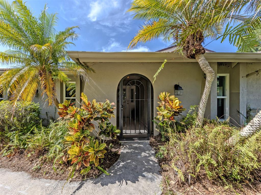 An arched front entryway with a metal security gate is surrounded by tropical landscaping — 750 SHETLAND CIRCLE, NOKOMIS, FL