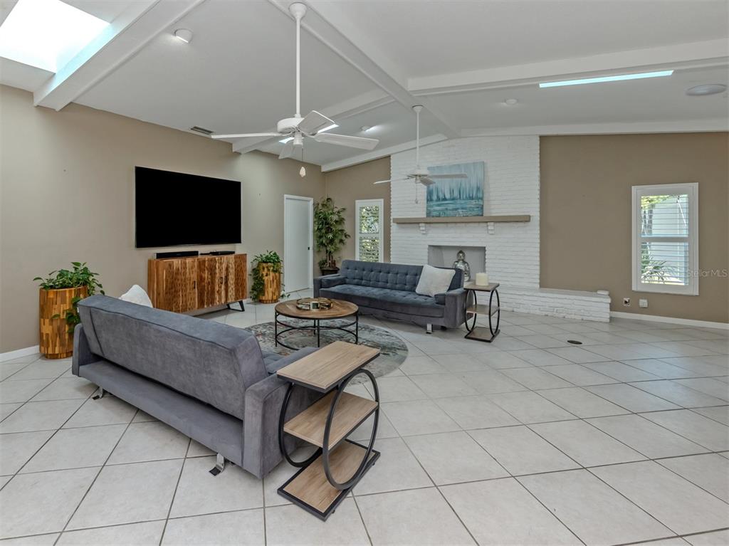 A spacious living room features a white brick fireplace, gray sofas, and tiled flooring — 750 SHETLAND CIRCLE, NOKOMIS, FL