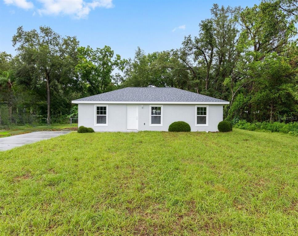 A single-story, light gray house with a white door and three windows sits on grass — 14719 SW 23RD PLACE, OCALA, FL