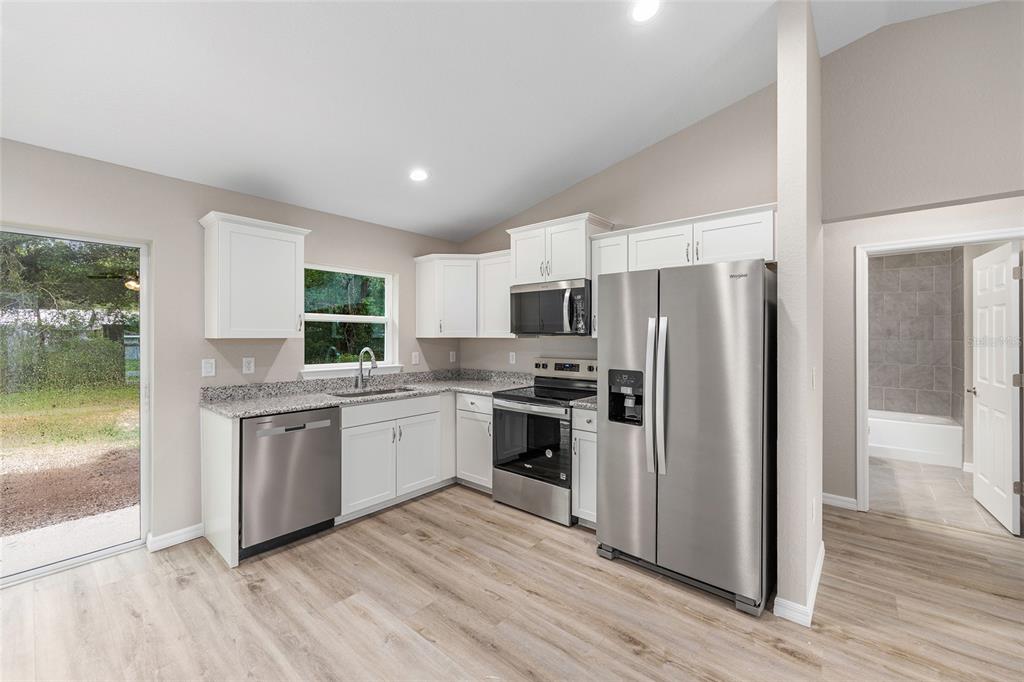 A kitchen with white cabinets, granite countertops, stainless steel appliances, and light wood-look flooring — 14719 SW 23RD PLACE, OCALA, FL