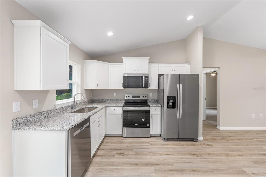 A kitchen with white cabinets, granite countertops, stainless steel appliances, and light wood-look flooring — 14719 SW 23RD PLACE, OCALA, FL