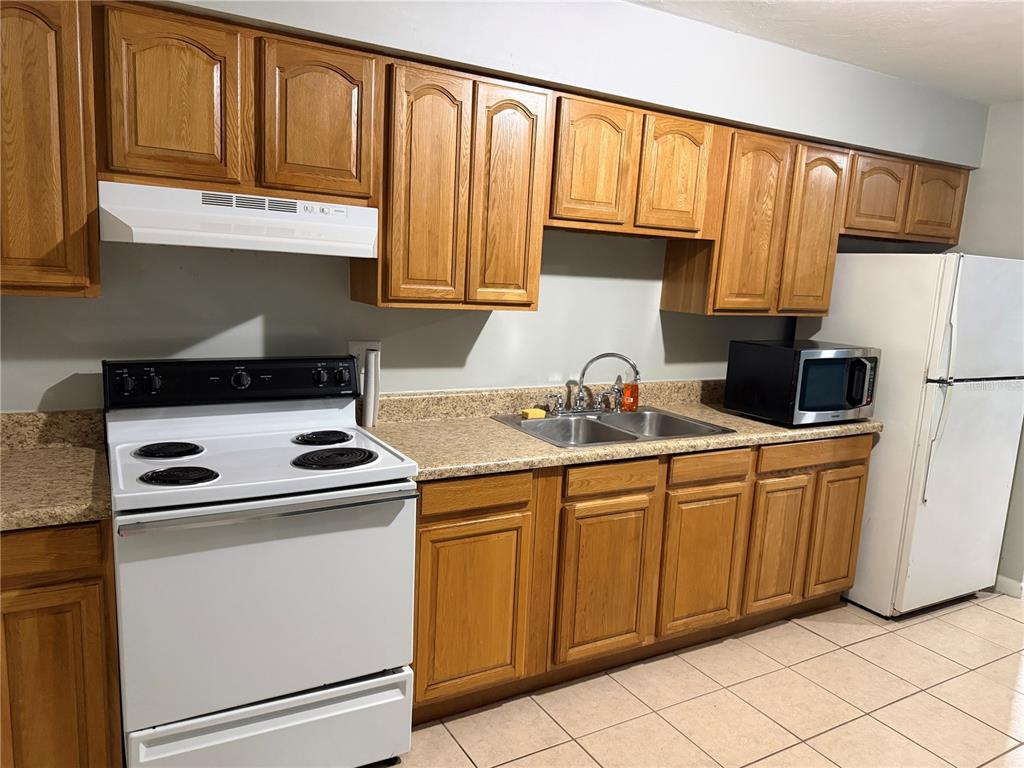 A kitchen features oak cabinets, white appliances, a double sink, and tan tile flooring — 2003 NW 31ST AVENUE, GAINESVILLE, FL