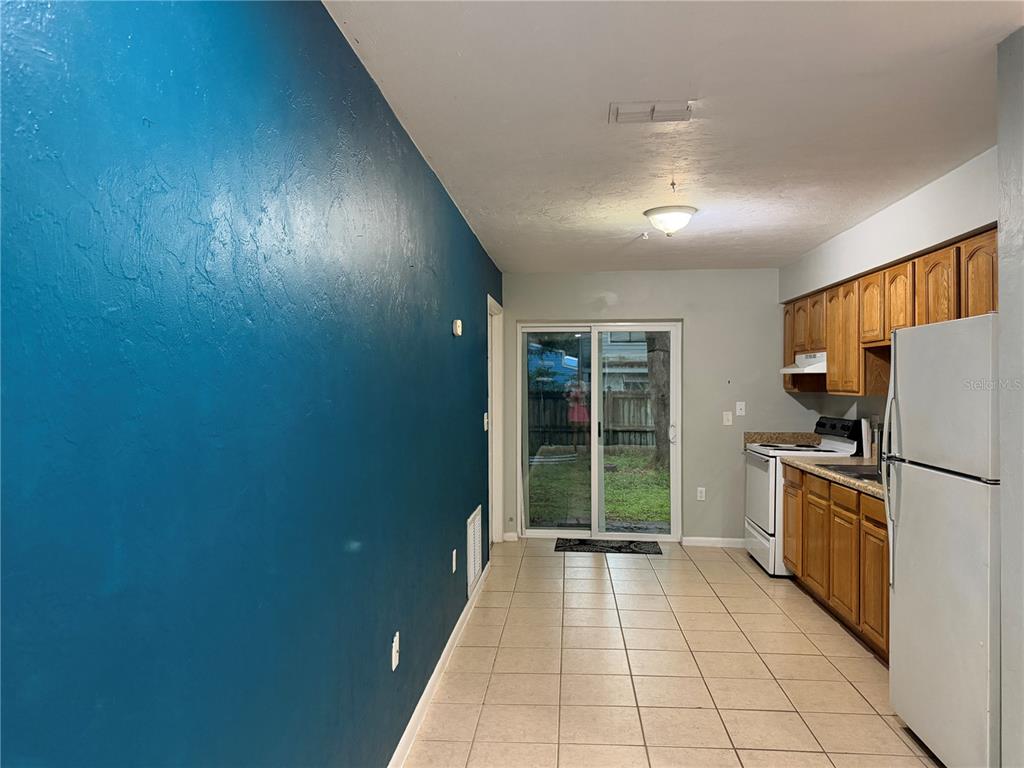 A kitchen with wood cabinets, white appliances, and a blue accent wall leads to a patio — 2003 NW 31ST AVENUE, GAINESVILLE, FL
