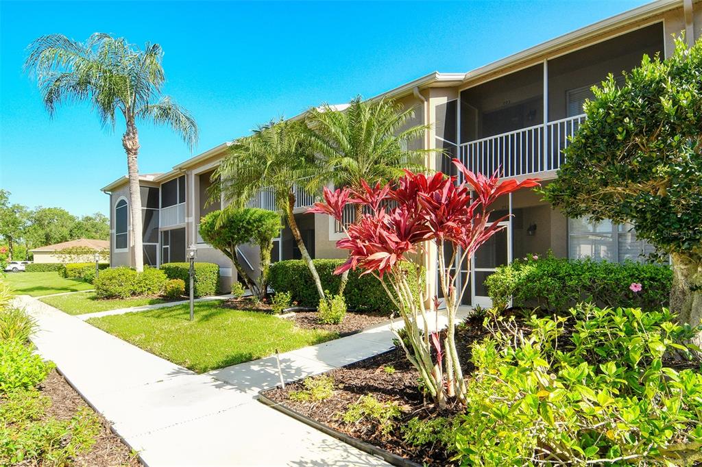 A two-story apartment building exterior features a screened balcony, palm trees, and landscaped garden beds — 5271 MAHOGANY RUN AVENUE UNIT 712, SARASOTA, FL