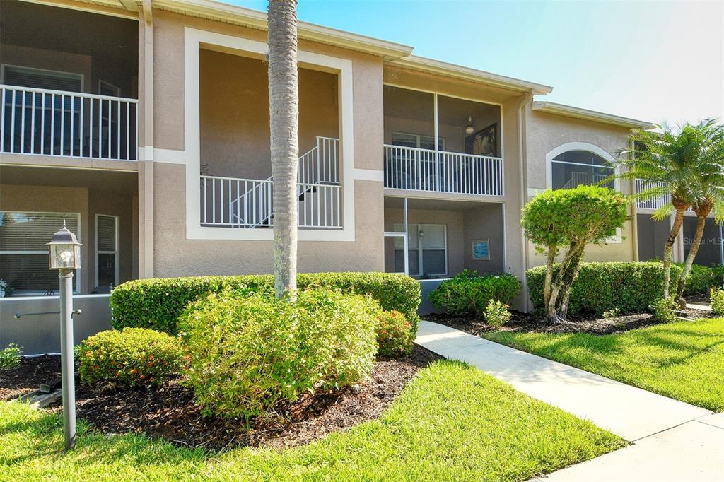 A two-story apartment building features tan stucco walls, screened balconies, and landscaped front grounds — 5271 MAHOGANY RUN AVENUE UNIT 712, SARASOTA, FL