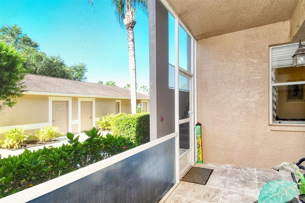A screened-in patio with tiled flooring overlooks a landscaped courtyard and neighboring residential buildings — 5271 MAHOGANY RUN AVENUE UNIT 712, SARASOTA, FL
