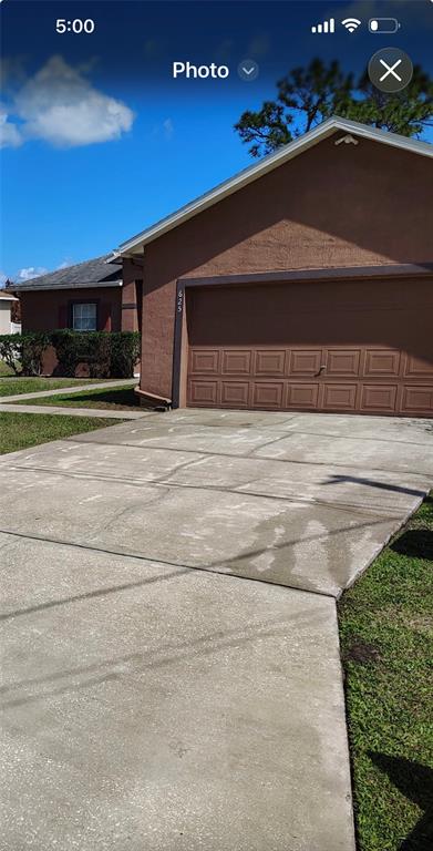 A brown house with a garage and a concrete driveway under a blue sky — 625 S DELMONTE COURT, KISSIMMEE, FL