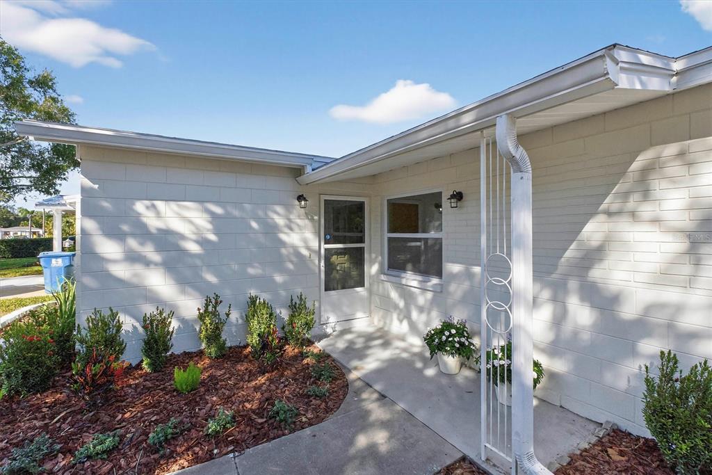 A white concrete block house exterior features a front entrance, walkway, and landscaped garden bed — 5701 14TH AVENUE N, ST PETERSBURG, FL