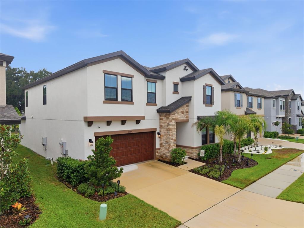 A two-story suburban house with a tan stucco exterior, stone accents, and a two-car garage — 14759 GALLOP RUN DRIVE, LITHIA, FL