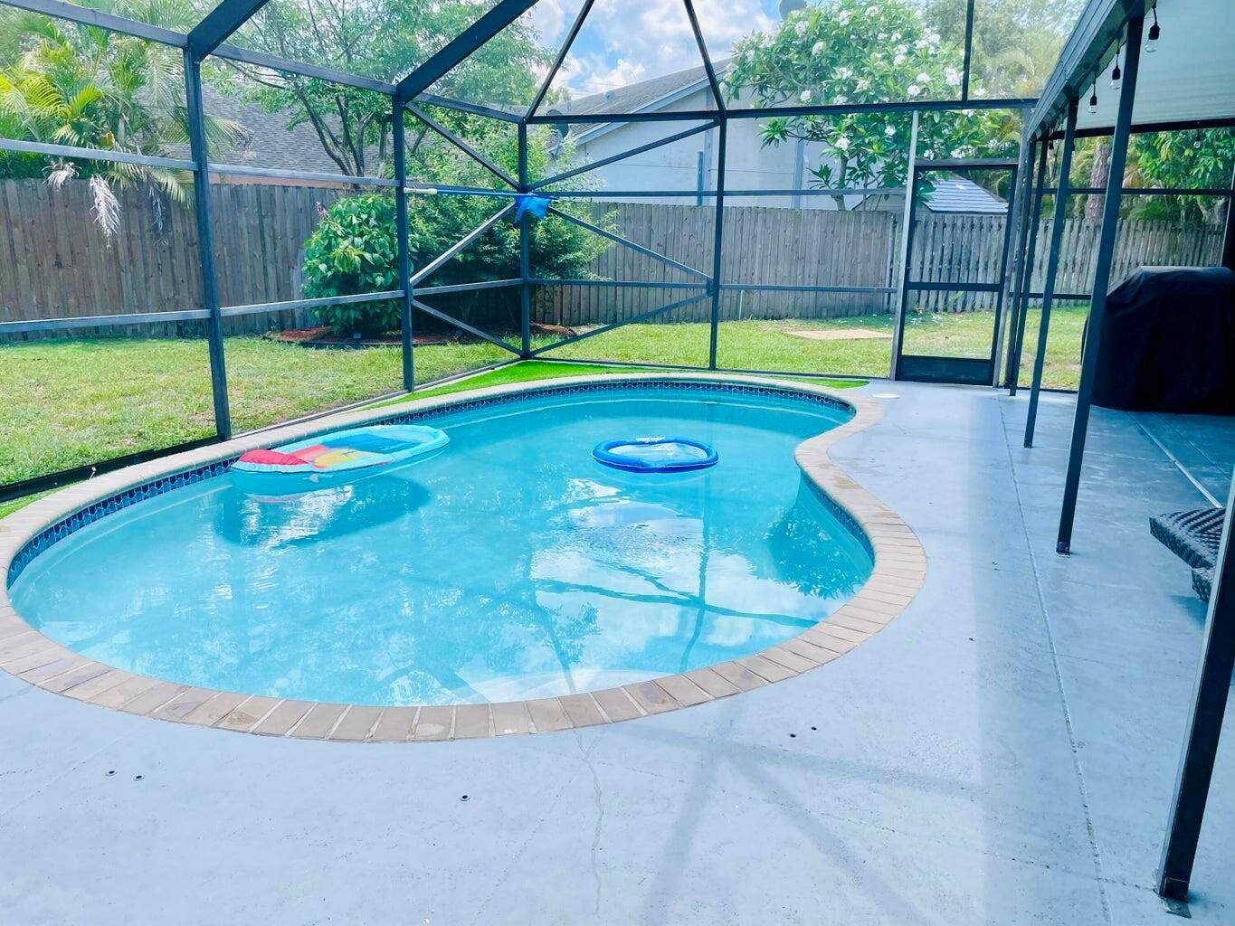 A kidney-shaped swimming pool sits inside a screened-in patio enclosure with a concrete deck — 1317 Periwinkle Place, Wellington FL 33414, WELLINGTON, FL