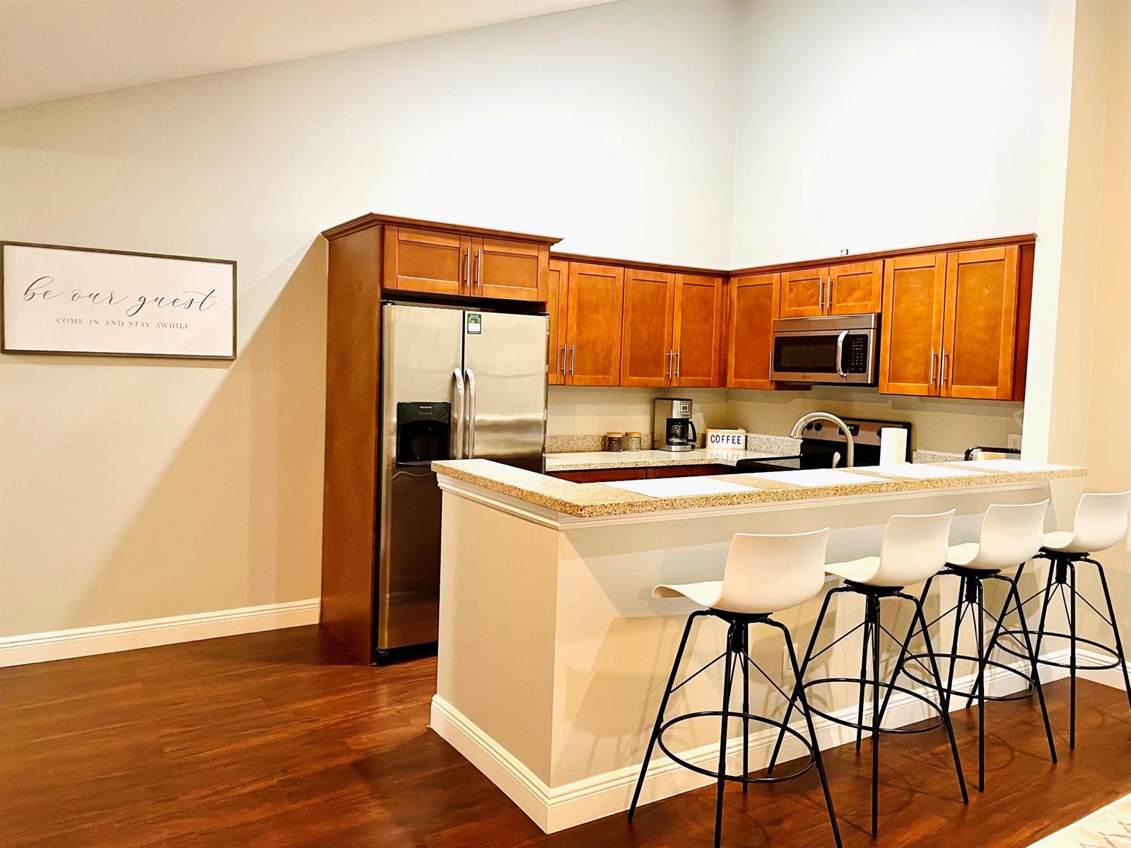 A kitchen features wooden cabinets, stainless steel appliances, a granite countertop, and four bar stools — 1317 Periwinkle Place, Wellington FL 33414, WELLINGTON, FL
