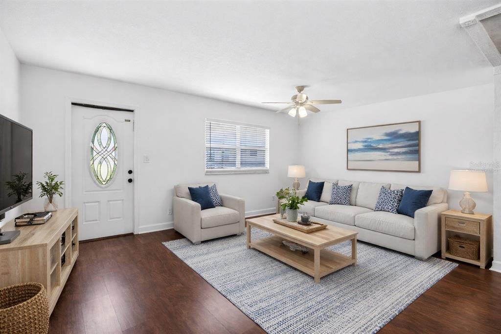 A living room with white walls, dark wood floors, a sofa, armchair, and area rug — 1801 BEDFORD LANE UNIT 27, SUN CITY CENTER, FL