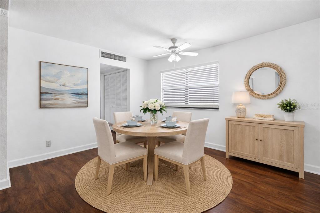 A dining room features a round wooden table, four chairs, and a circular wall mirror — 1801 BEDFORD LANE UNIT 27, SUN CITY CENTER, FL