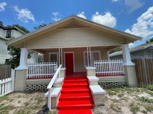 A tan bungalow features a prominent red front door and matching red porch steps — 221 W EMILY STREET, TAMPA, FL