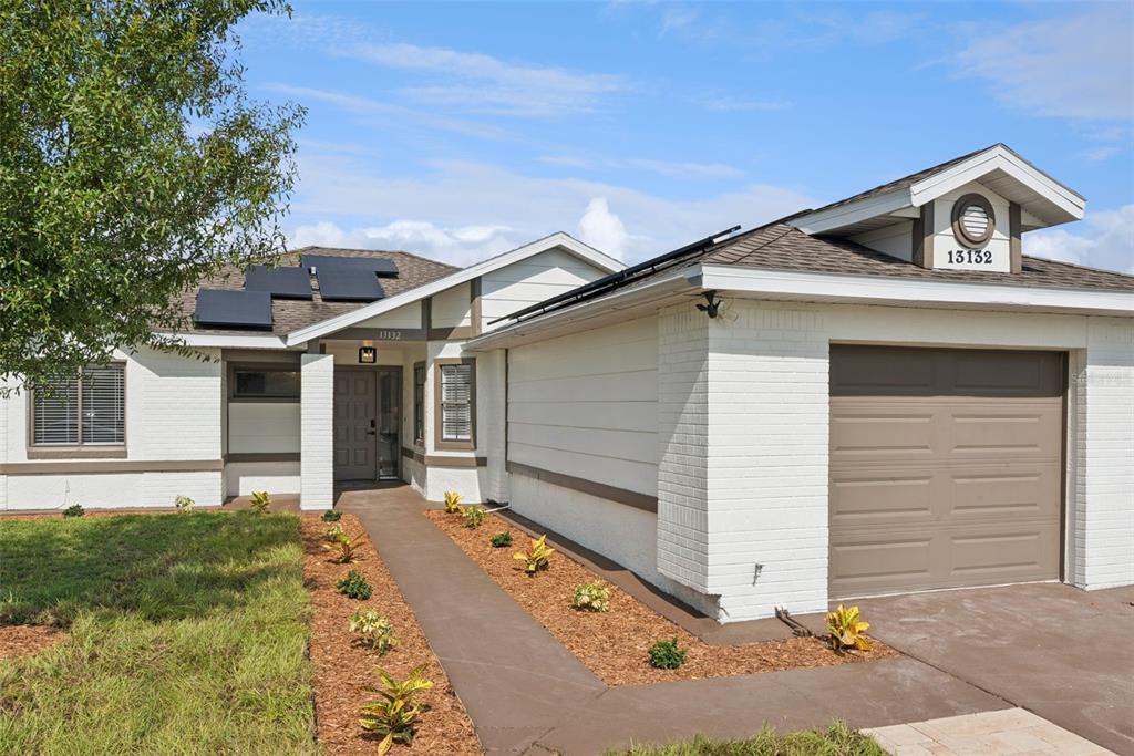 A single-story house features a white brick facade, a brown garage door, and solar panels — 13132 PHOENIX WOODS LANE, ORLANDO, FL