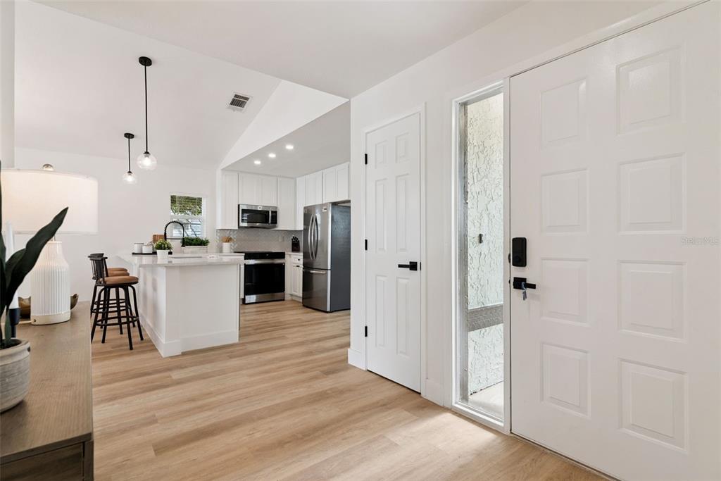 A bright entryway leads into an open-concept kitchen with white cabinetry and wood-look flooring — 13132 PHOENIX WOODS LANE, ORLANDO, FL