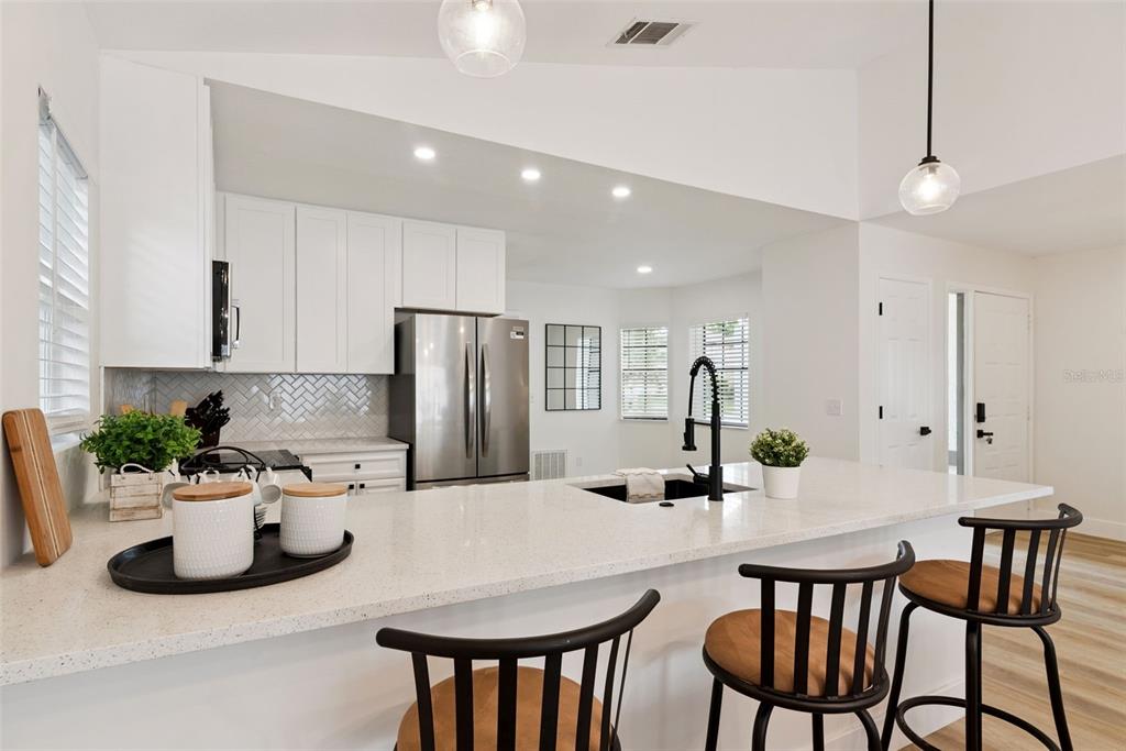 A modern kitchen features white cabinets, a quartz island with bar seating, and stainless appliances — 13132 PHOENIX WOODS LANE, ORLANDO, FL