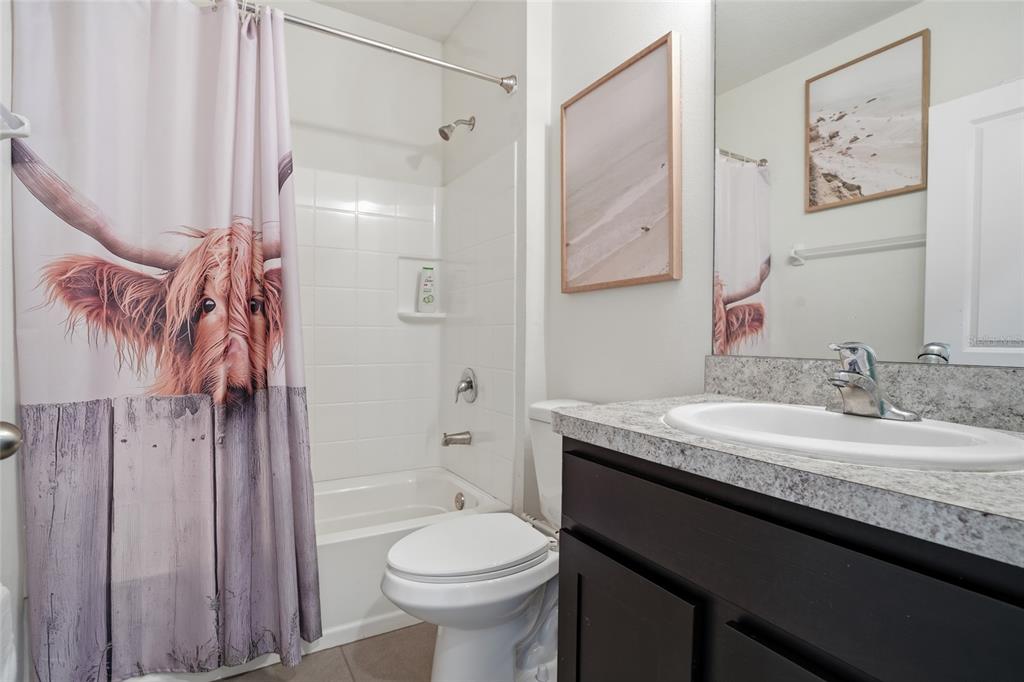 A bathroom features a shower-tub combo with a highland cow curtain, toilet, and vanity sink — 35803 HILLBROOK AVENUE, ZEPHYRHILLS, FL