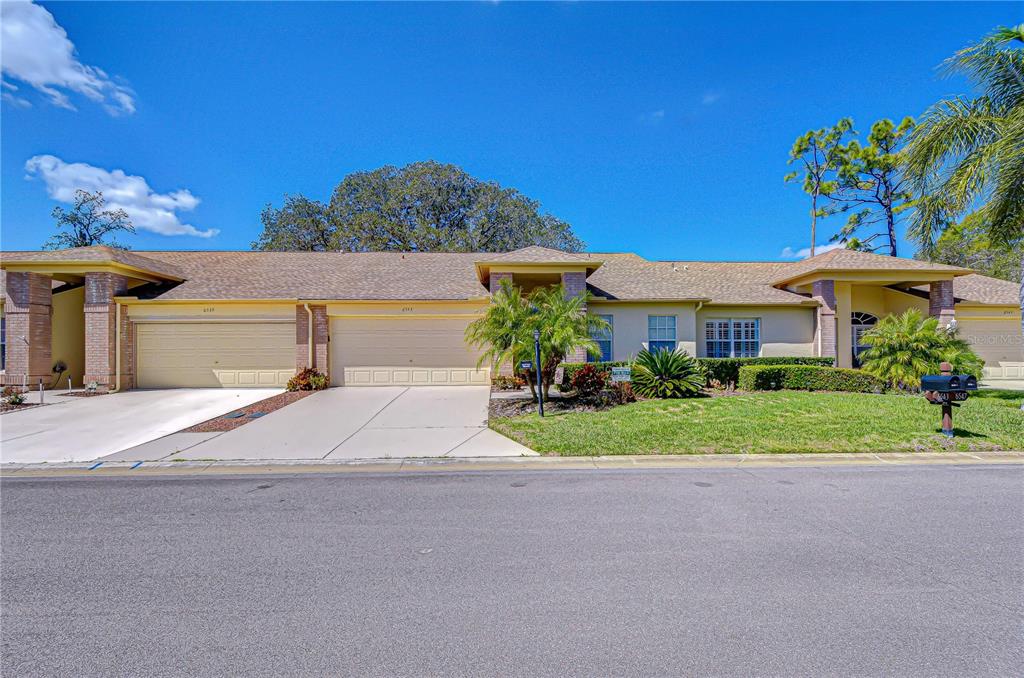 A single-story duplex with two garages, a tan exterior, and a manicured front lawn — 6543 PINE WALK DRIVE, NEW PORT RICHEY, FL