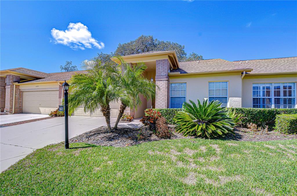 A single-story house with a beige stucco exterior, a two-car garage, and front landscaping — 6543 PINE WALK DRIVE, NEW PORT RICHEY, FL