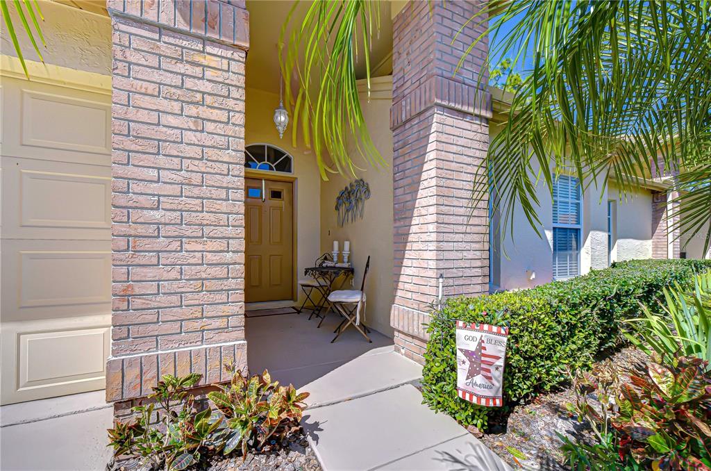 A front entryway features a tan door, brick columns, and a small bistro set — 6543 PINE WALK DRIVE, NEW PORT RICHEY, FL