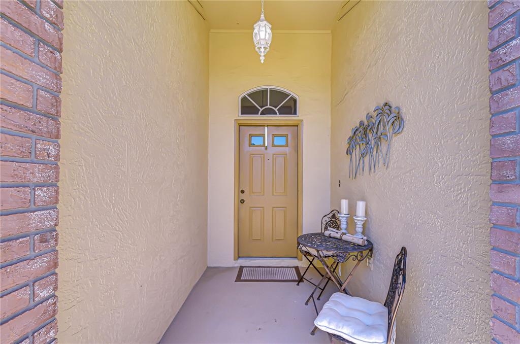 A covered entryway features a tan front door, brick columns, and a small bistro set — 6543 PINE WALK DRIVE, NEW PORT RICHEY, FL