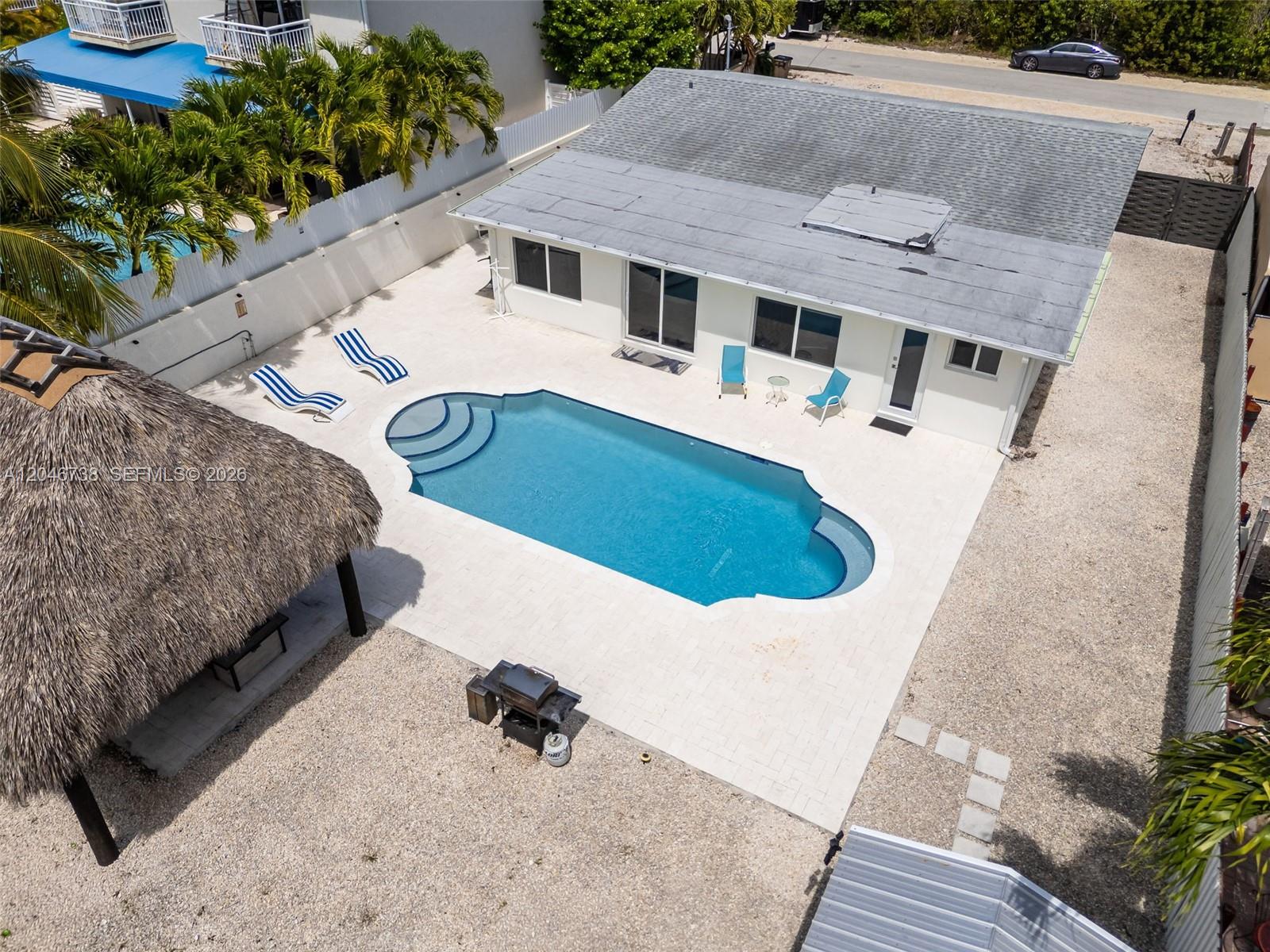 An aerial view shows a backyard with a swimming pool, patio, and thatched-roof structure — 16 Fishermans Trl, Key Largo FL 33037, KEY LARGO, FL