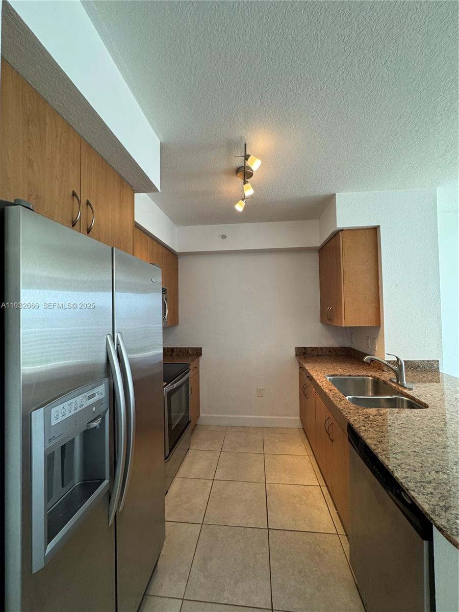 A galley kitchen features wood cabinets, granite countertops, stainless steel appliances, and tile flooring — 1830 Radius Dr # 915, Hollywood FL 33020, HOLLYWOOD, FL