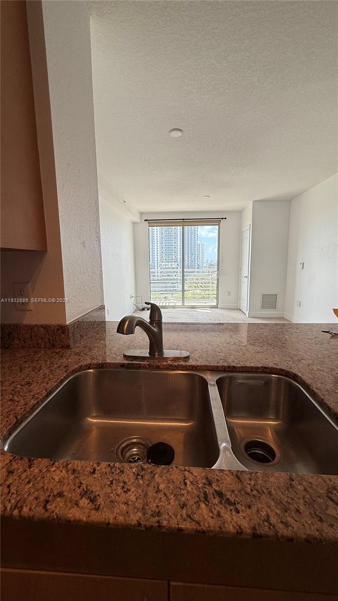 A kitchen sink with a granite countertop overlooks a living area with a balcony door — 1830 Radius Dr # 915, Hollywood FL 33020, HOLLYWOOD, FL