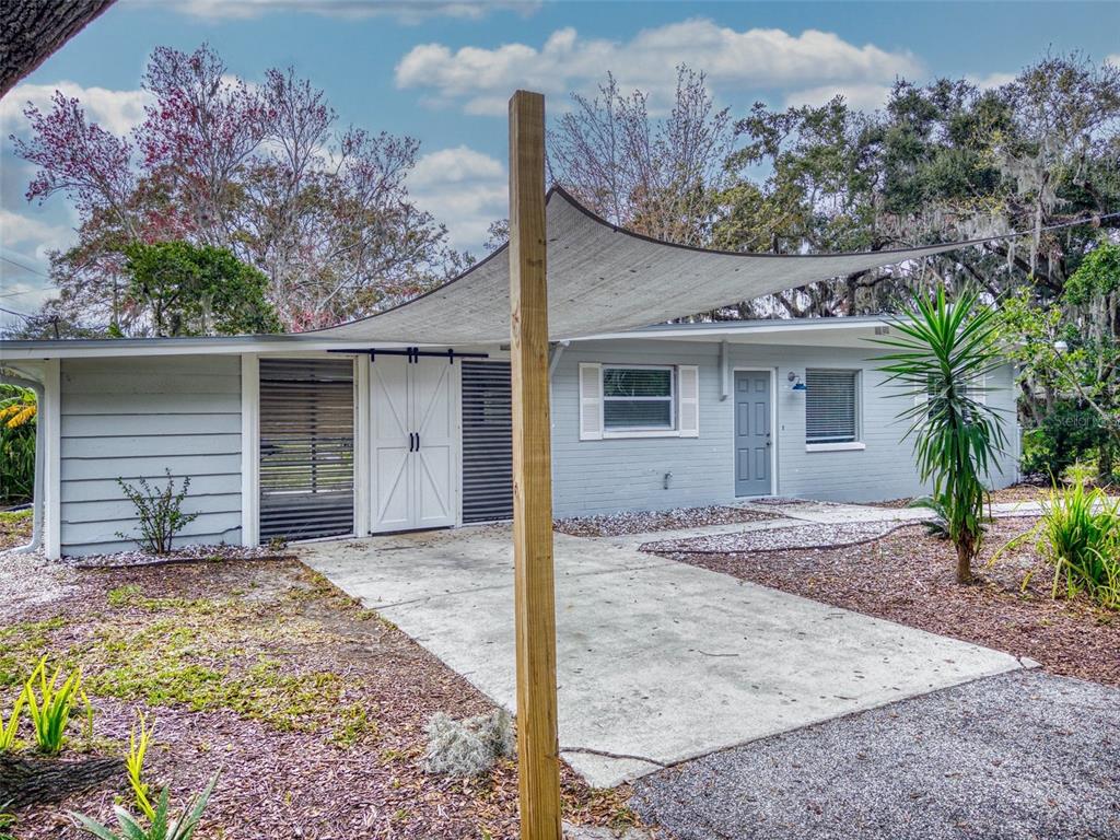 A light gray house exterior features a concrete driveway covered by a large shade sail — 104 FRAN DRIVE, NEW SMYRNA BEACH, FL