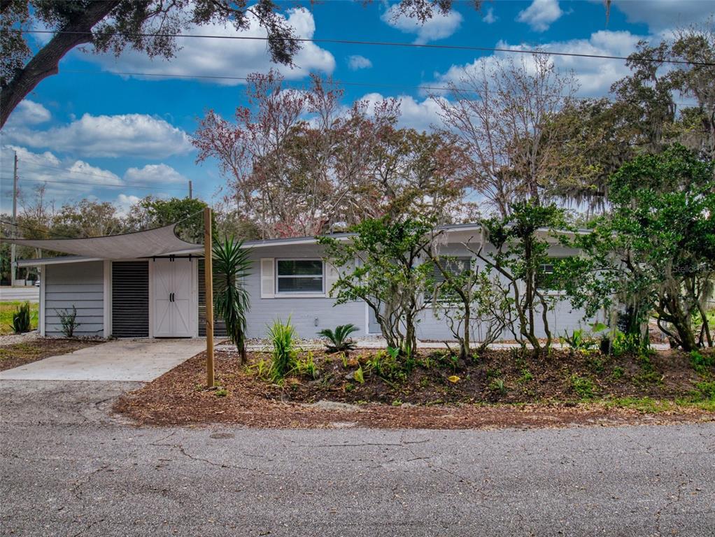 A single-story light gray house with a white barn-style door and a shade sail canopy — 104 FRAN DRIVE, NEW SMYRNA BEACH, FL