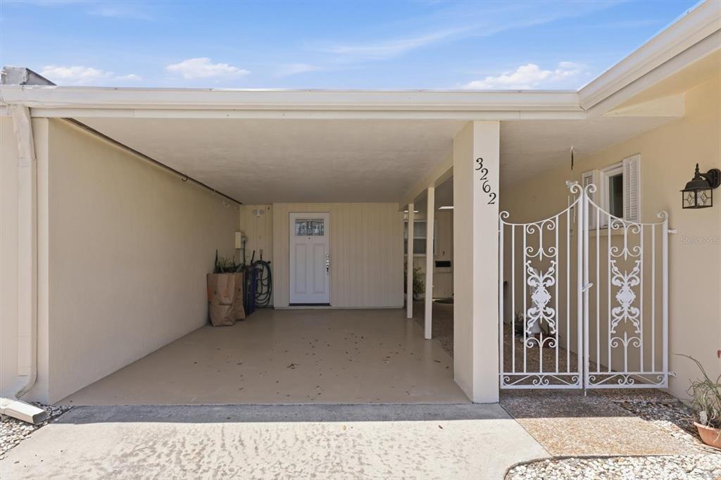 A covered carport features a white door, a decorative metal gate, and a concrete floor — 3262 BROCKTON LANE UNIT 608, SARASOTA, FL