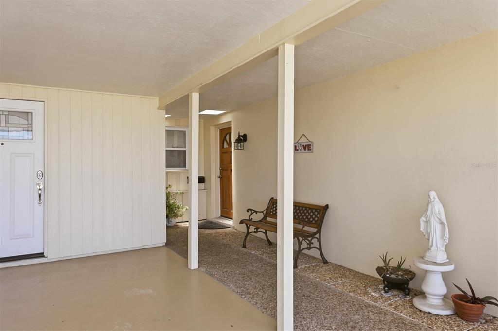 A covered porch features a white door, two benches, and a statue on a pedestal — 3262 BROCKTON LANE UNIT 608, SARASOTA, FL