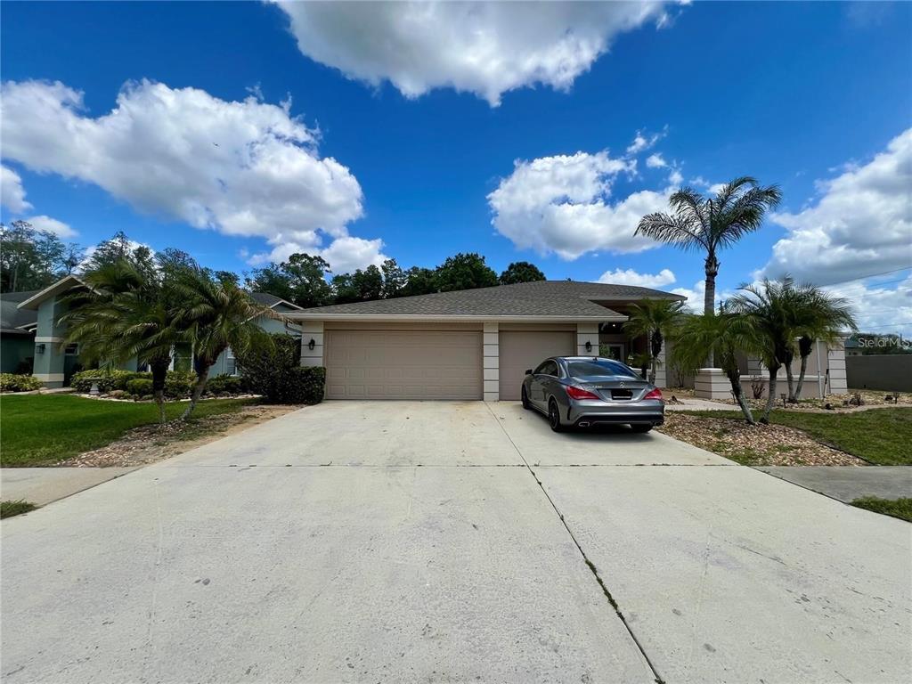 A single-story house with a three-car garage and a gray sedan parked in the driveway — 5810 REDHAWK DRIVE, NEW PORT RICHEY, FL